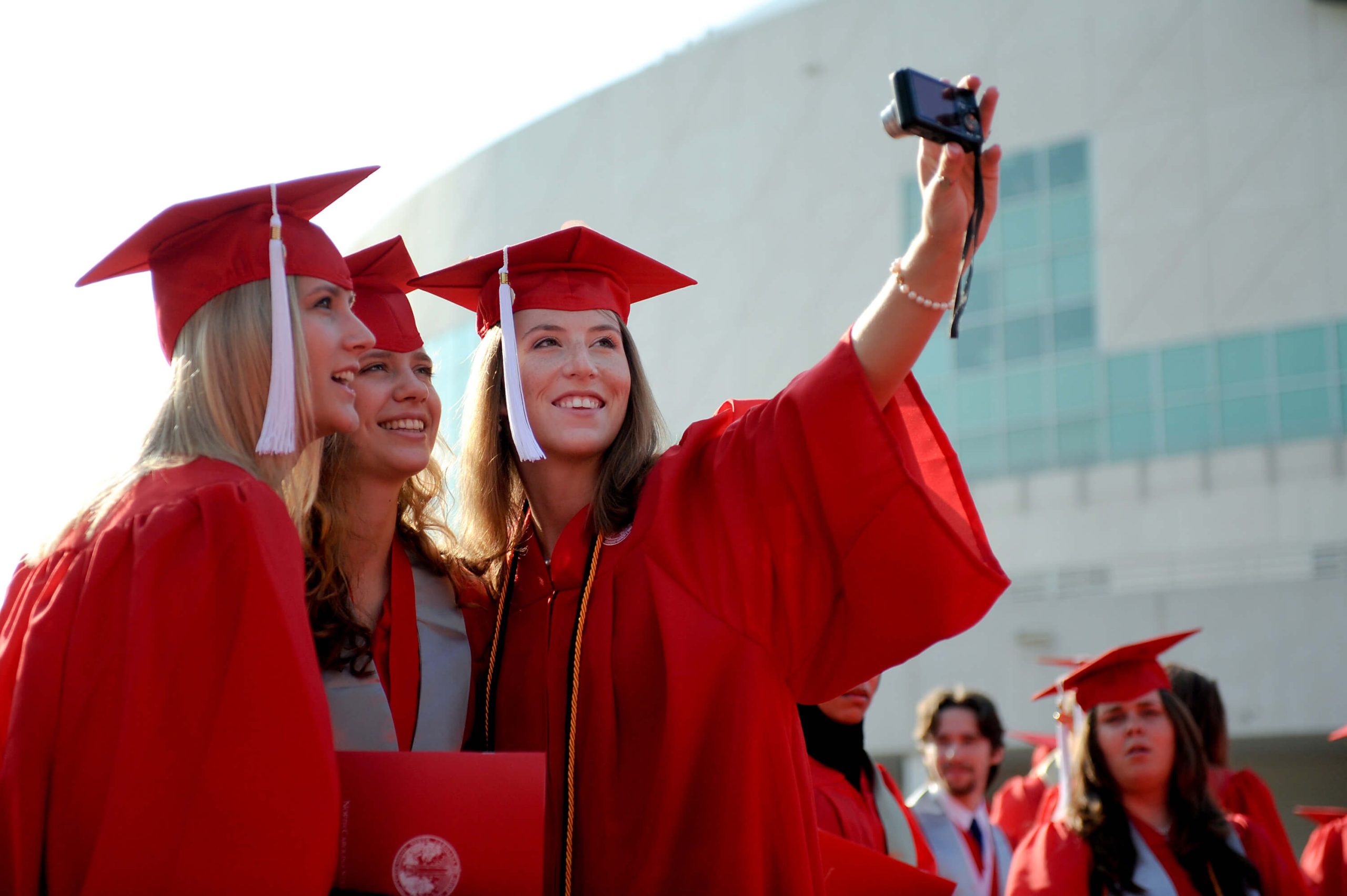 Three students in cap and gowns taking a selfie outside