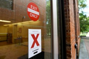 Glass door with "exit only" sign and additional sign directing user to the correct entrance