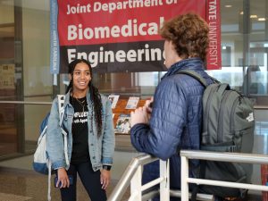 two students talking and standing in front of a joint department biomedical engineering sign